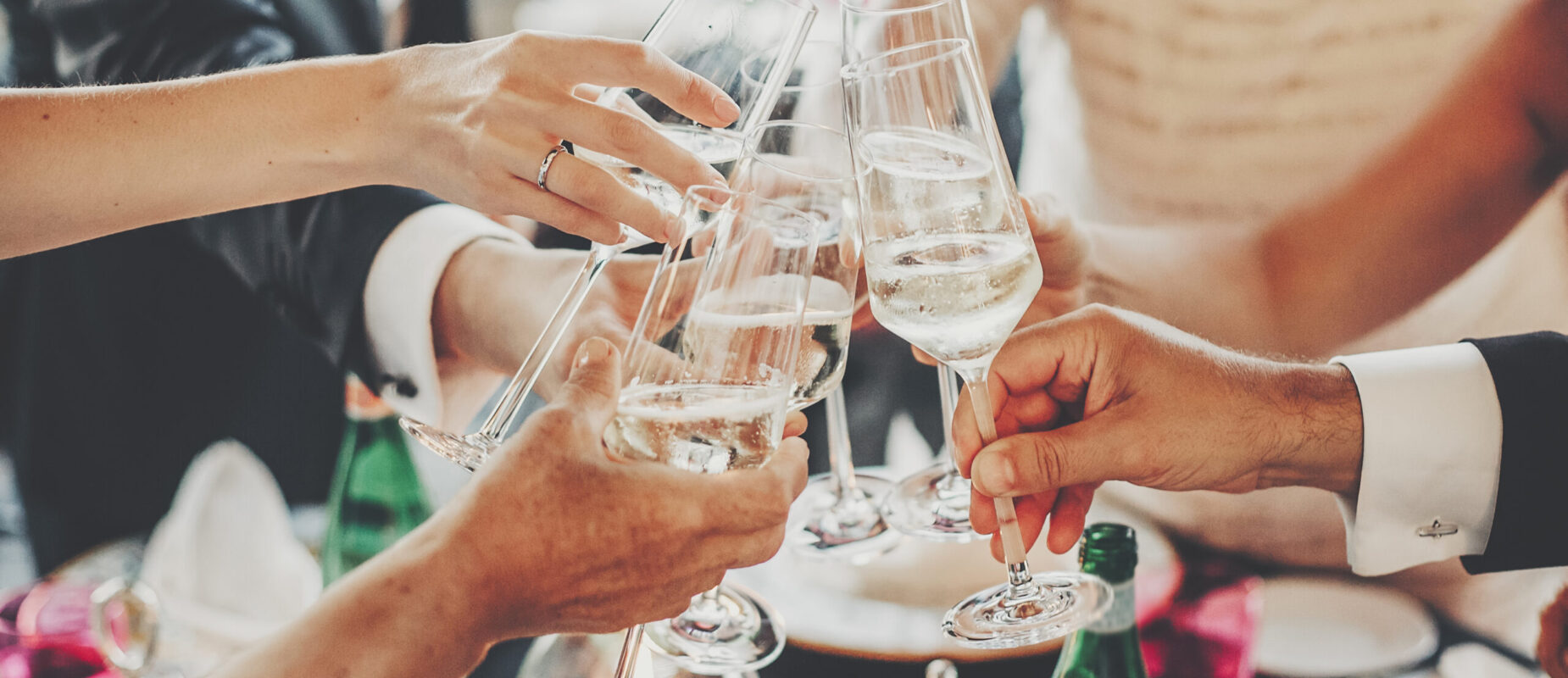 Hands toasting with champagne glasses at wedding reception outdoors in the evening. Family and friends clinking glasses and cheering with alcohol at delicious feast celebration. Christmas party